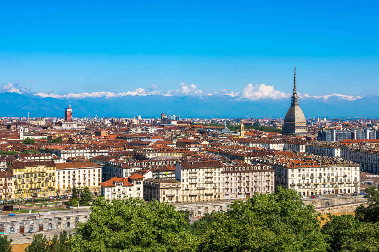 A panoramic view of Turin, Italy, showcasing the Mole Antonelliana tower against a backdrop of the Alps.
